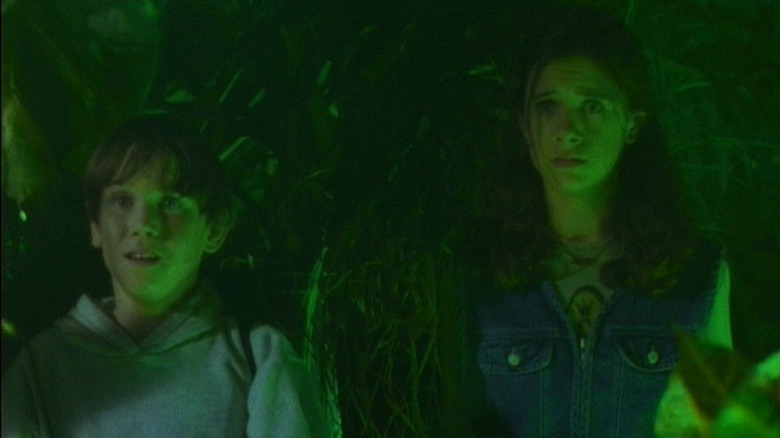 Casey (Blake McGrath) and Margaret Brewer (Beki Lantos) stand in a leafy green-lit basement in Goosebumps (1995)