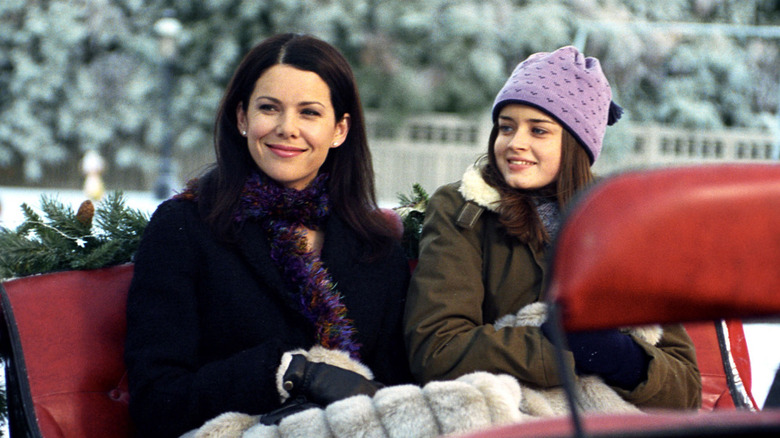 Lauren Graham as Lorelai Gilmore and Alexis Bledel as Rory Gilmore in Gilmore Girls, sitting out in a sleigh in the snow and smiling at something off camera