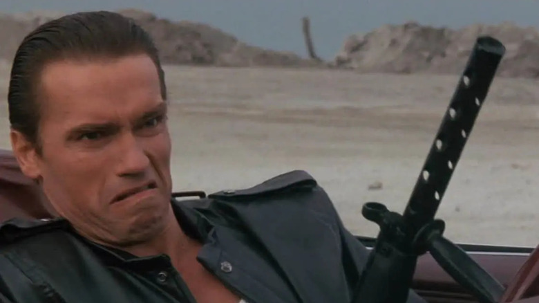 Mark Kaminski (Arnold Schwarzenegger) makes a face while driving and hold a gun in Raw Deal