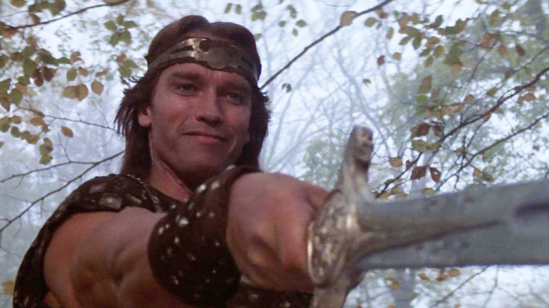 Kalidor (Arnold Schwarzenegger) smiles while holding out a sword in Red Sonya (1985)
