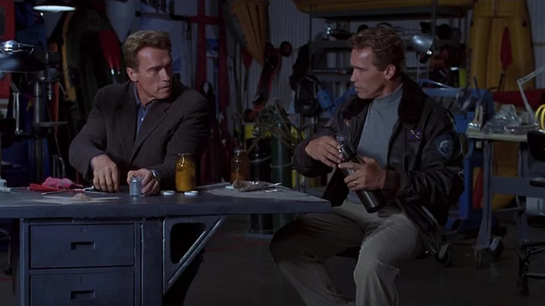 Adam Gibson (Arnold Schwarzenegger) speaks with his identical clone while seated at a desk in The 6th Day