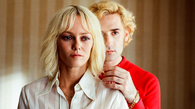 A woman stands in front of a man in a red sweater in Knife+Heart