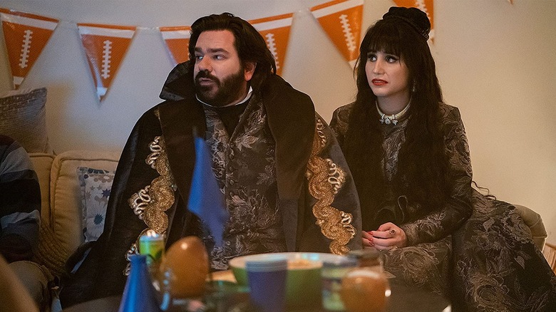 Laszlo and Nadja sit on a couch, football banner behind them