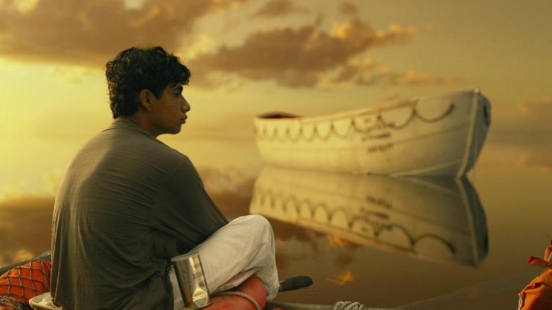 Suraj Sharma as Pi Patel sitting on a lifebuoy tied to a boat in Life of Pi