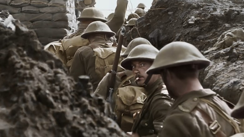 World War I soldiers walking through trenches while one looks at the camera in They Shall Not Grow Old