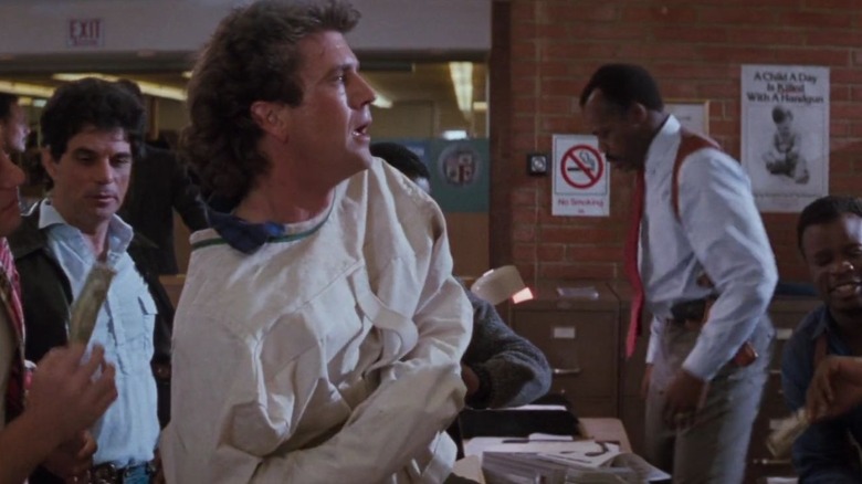 Mel Gibson as Riggs demonstrates his straitjacket-escape skills, as Murtaugh (Danny Glover) tries to be more serious, in Lethal Weapon 2