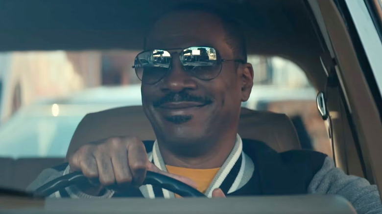 Eddie Murphy as Axel Foley, smiling with shades on while he drives a car in Beverly Hills Cop: Axel F