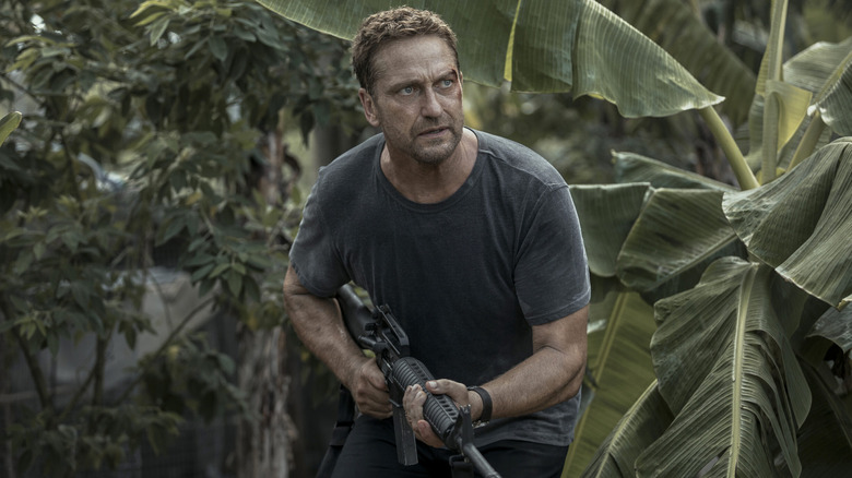 Gerard Butler as Brodie Torrance, walking through a jungle with an assault rifle in Plane