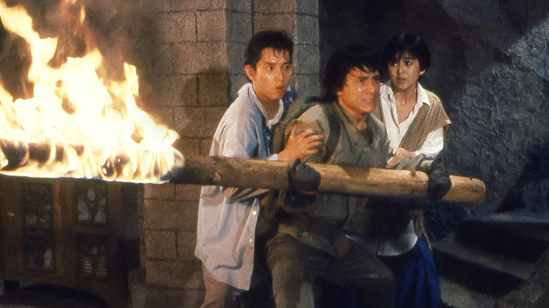 Jackie (Jackie Chan) holds a flaming log in front of Alan (Alan Tam) and Lorelei (Rosamund Kwan) in Armour of God