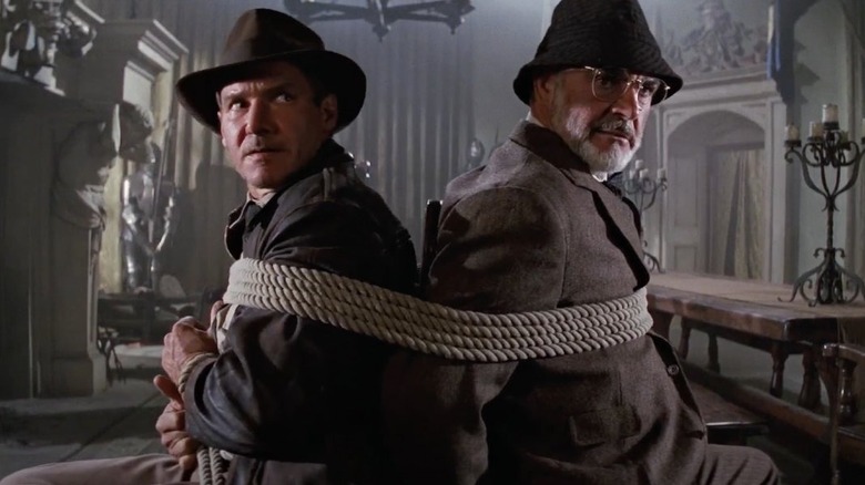 Indiana Jones (Harrison Ford) and Henry Jones (Sean Connery) are tied back-to-back in chairs in Indiana Jones and the Last Crusade