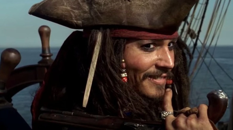 Jack Sparrow (Johnny Depp) grins looking over his shoulder while holding a pistol in Pirates of the Caribbean: The Curse of the Black Pearl