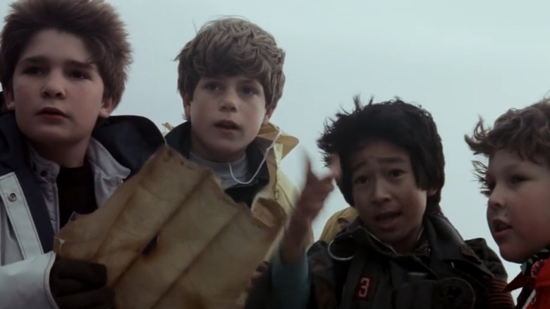 Mouth (Corey Feldman), Mikey (Sean Astin), Data (Ke Huy Quan), and Chunk (Jeff Cohen) stand outside with a treasure map in The Goonies