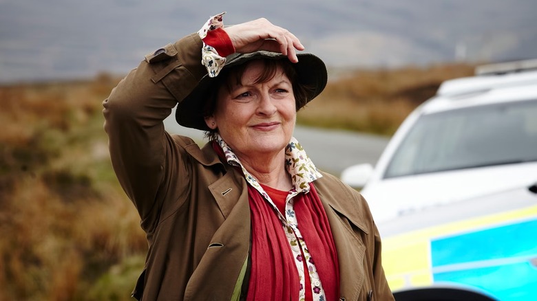 Vera Stanhope (Brenda Blethyn) holds her hat by a police car in Vera