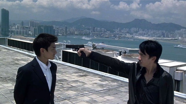 Chan Wing-yan (Tony Leung) points a pistol directly at the head of Lau Kin-ming (Andy Lau) on a roof overlooking Hong Kong in Infernal Affairs