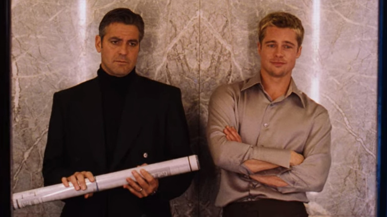 Danny Ocean (George Clooney) holds a schematic next to a smirking Rusty Ryan (Brad Pitt) in Ocean's Eleven (2001)