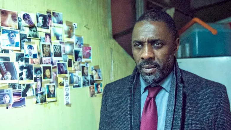 John Luther (Idris Elba) stands by a wall of Polaroid photographs in Luther