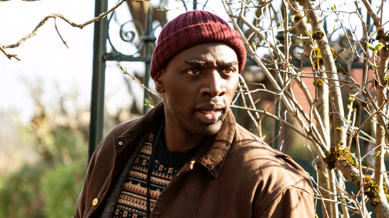Omar Sy as Assane Diop, peering through trees in Lupin