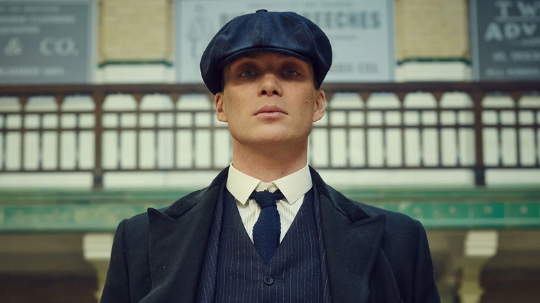 Cillian Murphy as Thomas Shelby, standing with his cap pulled over his eyes in Peaky Blinders