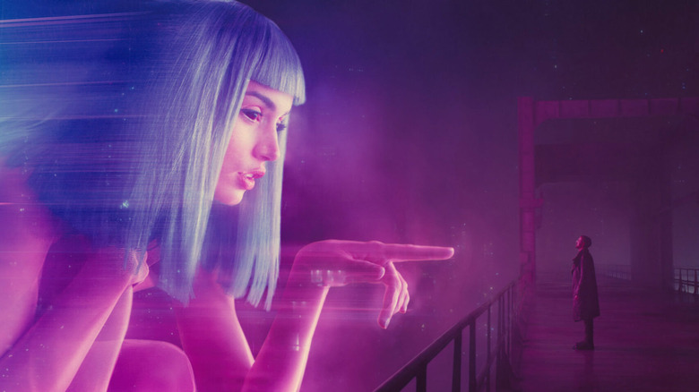 K (Ryan Gosling) stares at a gigantic holographic projection of Joi (Ana de Armas) pointing at him in Blade Runner 2049