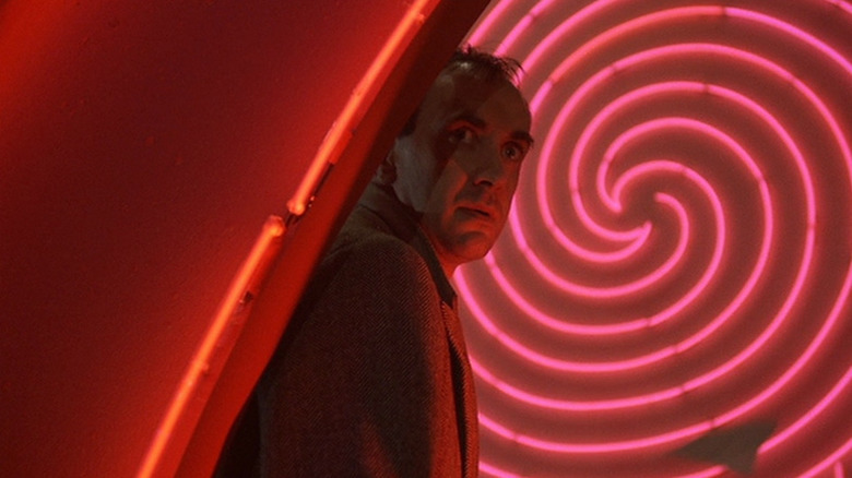 Sam Lowry (Jonathan Pryce) stands in front of a red swirl neon light in Brazil