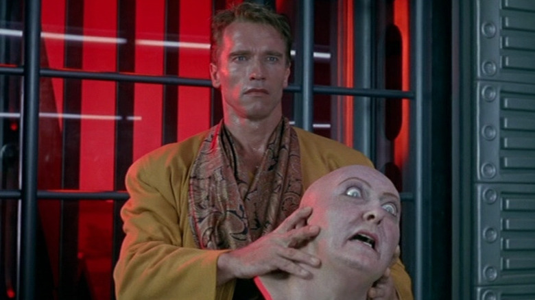 Douglas Quaid (Arnold Schwarzenegger) stands with an animatronic femake head in his hands in Total Recall