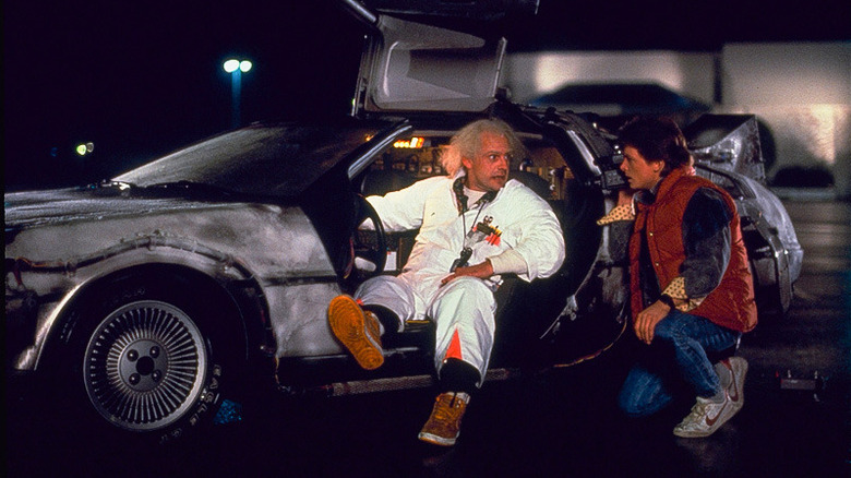 Marty McFly (Michael J. Fox) speaks to Doc Brown (Christopher Lloyd) by an open DeLorean in Back to the Future