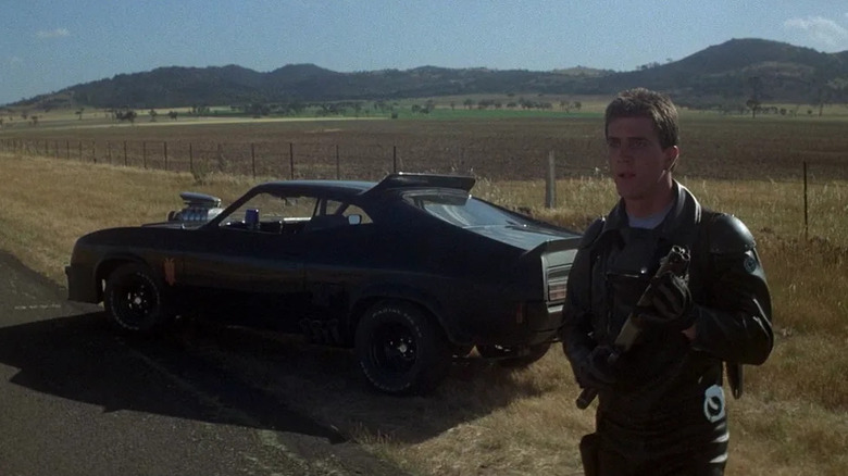 Max Rockatansky (Mel Gibson) stands next to the V8 Interceptor on the side of the road in Mad Max