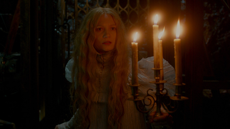 Mia Wasikowska as Edith,holding candles in a dark hallway in Crimson Peak