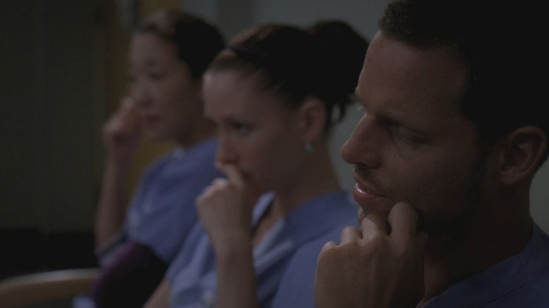 Sandra Oh as Dr. Cristina Yang, Chyler Leigh as Dr. Lexie Grey, and Justin Chambers as Dr. Alex Karev sitting side by side with pensive expressions on Grey's Anatomy