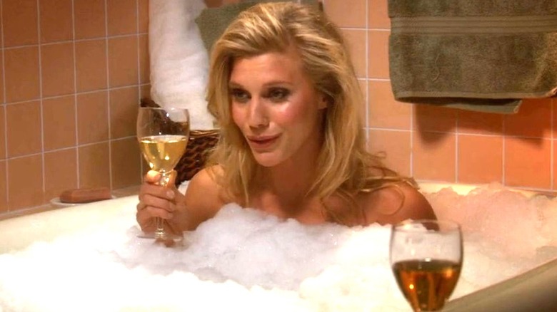 Katee Sackhoff as herself sits in a bathtub and holds a champagne glass while talking on The Big Bang Theory