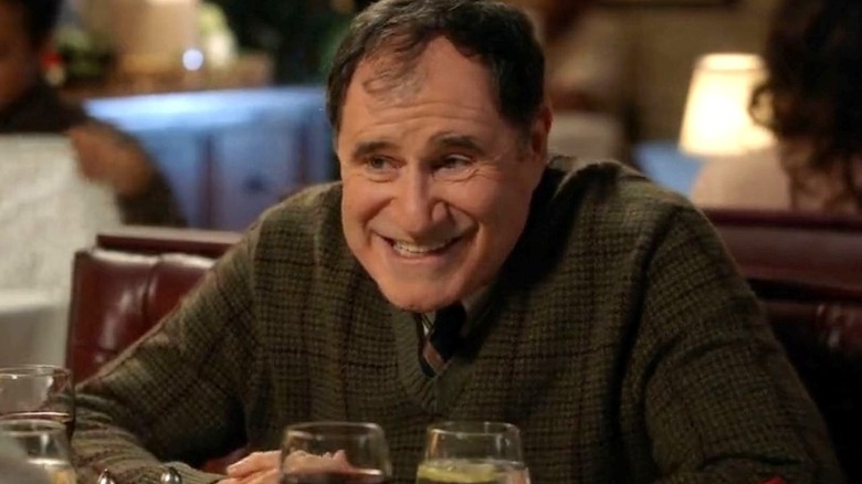 Richard Kind as Ira Rosenbloom sits at a restaurant table and smiles on Young Sheldon