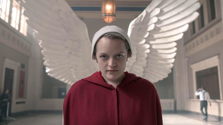 Elisabeth Moss as Offred looks ahead with wings from a statue behind her on The Handmaid's Tale