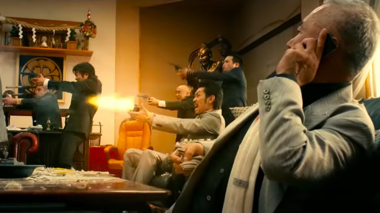 Jun Kunimura on the phone while thugs shoot guns