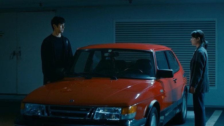 Yūsuke Kafuku (Hidetoshi Nishijima) faces Misaki Watari (Tōko Miura) in a garage with a car between them in Drive My Car