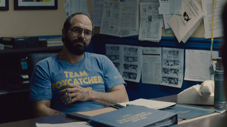 Dave Schultz (Mark Ruffalo) sits behind a desk holding a glass in Foxcatcher