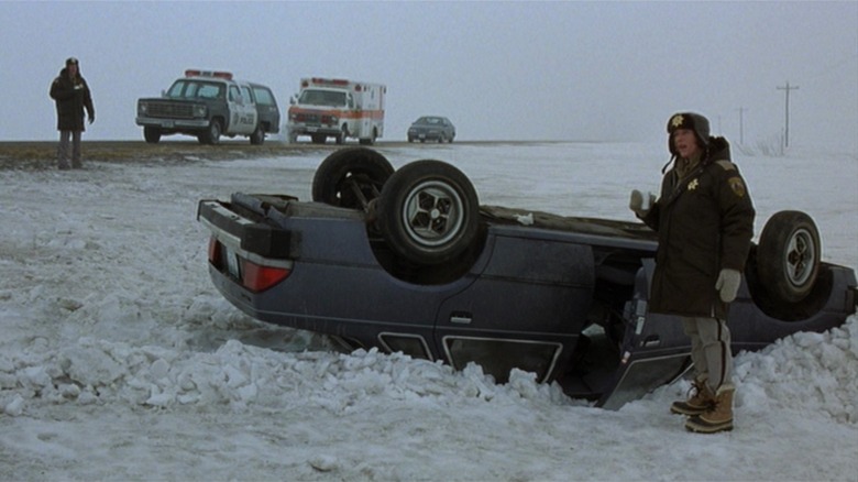 Francis McDormand as Marge Gunderson stands next to an overturned car in the snow, in Fargo