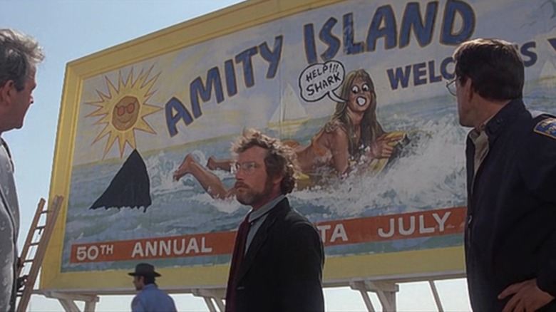 Richard Dreyfuss as Matt Hooper and Roy Scheider as Martin Brody standing in front of the defaced Amity Island billboard in Jaws