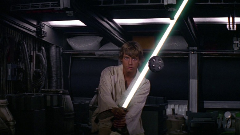 Mark Hamill as Luke Skywalker in Star Wars holds a lightsaber against a practice droid