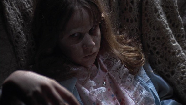 Linda Blair as Regan in The Exorcist, looking up at the camera with sunken-in eyes, her limp hand raised