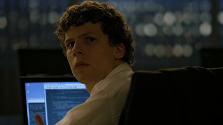 Jesse Eisenberg as Mark Zuckerberg turns around in his chair in The Social Network, code visible on his laptop screen