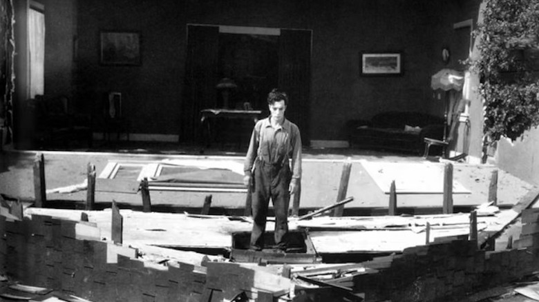 Buster Keaton standing in front of house with fallen facade in Steamboat Bill, Jr