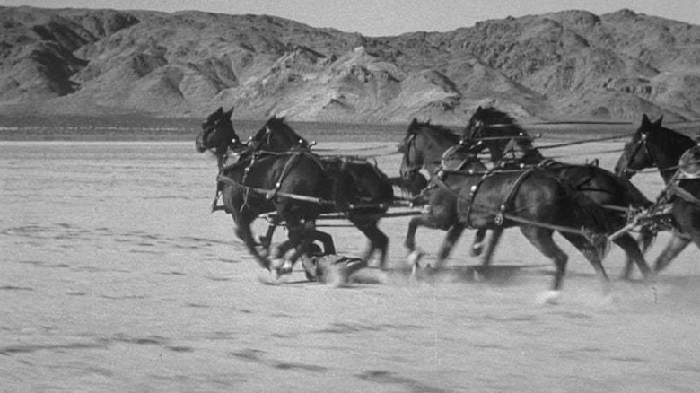 Stuntman Yakima Canutt (face not visible) hanging on to bar underneath six galloping horses in the desert in Stagecoach
