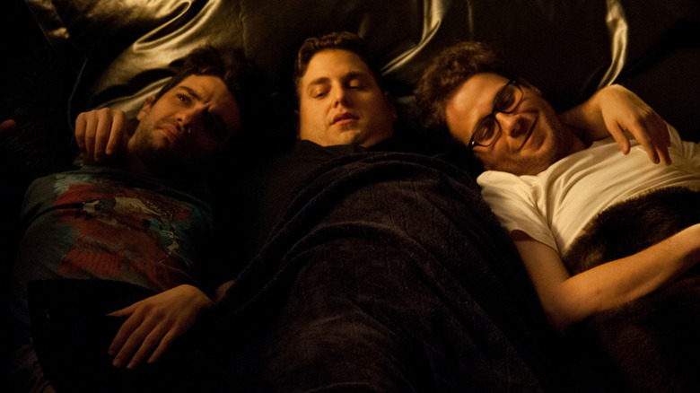 Jonah Hill as himself lying on a couch with his arms around Jay Baruchel and Seth Rogen in This Is The End