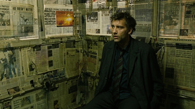 A bewildered Theo Faron (Clive Owen) sits in a room with newspapers on the walls in Children of Men