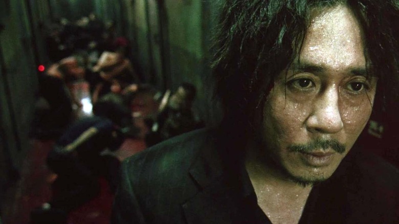 A sweaty Oh Dae-su (Choi Min-sik) stands in front of a hallway of battered crooks in Oldboy (2003)