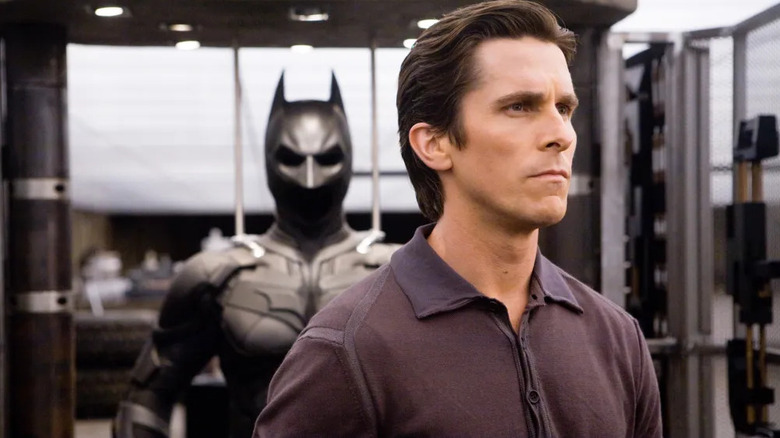 Bruce Wayne (Christian Bale) stands grimly in front of the Batsuit in The Dark Knight