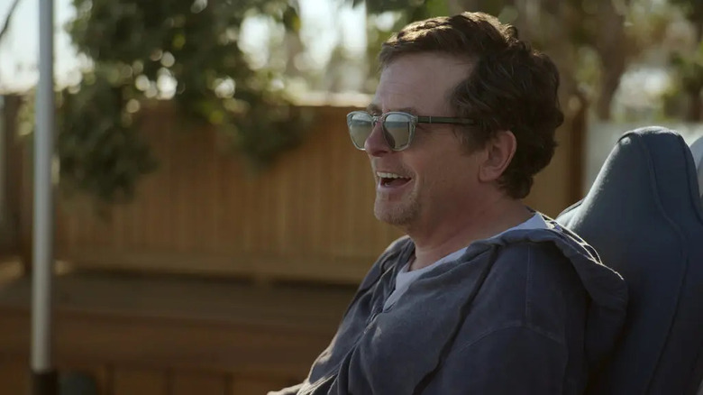 Michael J. Fox sitting in sunglasses and smiling in Still: A Michael J. Fox Movie