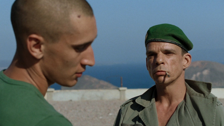 Denis Lavant as Galoup, in army green with cigarette, facing Grégoire Colin as Sentain, facing the side, in Beau travail