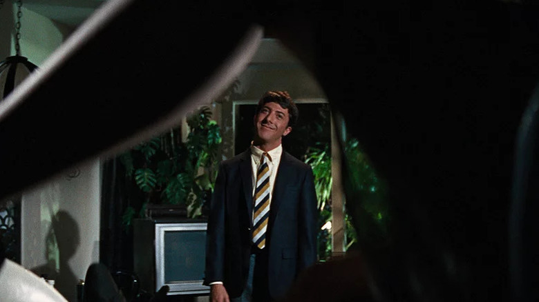 Dustin Hoffman as Benjamin smiling and framed underneath bent leg in shadow in The Graduate