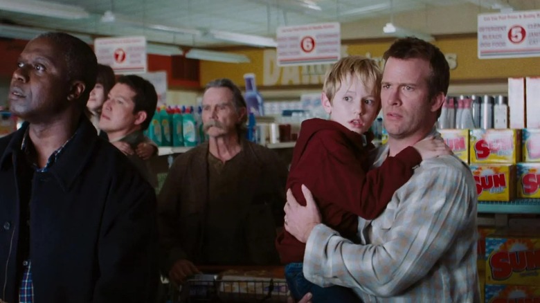 A bunch of survivors including Andre Braugher as Brent and Thomas Jane as David holding his son, staring out the windows of the grocery store in The Mist